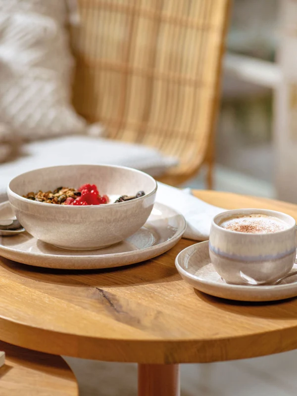 Eine Perlemor Tasse mit Kaffee und eine Schüssel mit Müsli auf einem Holztisch.