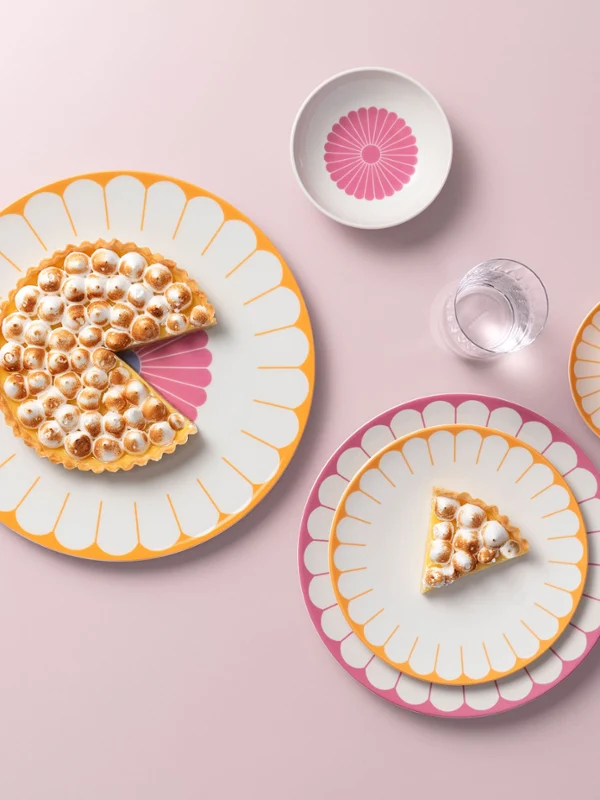 Gâteau entamé sur des assiettes décoratives, accompagné d'une petite fourchette, d'un verre d'eau et d'une tasse sur fond rose. Gâteau entamé sur des assiettes décoratives, accompagné d'une petite fourchette, d'un verre d'eau et d'une tasse sur fond rose.