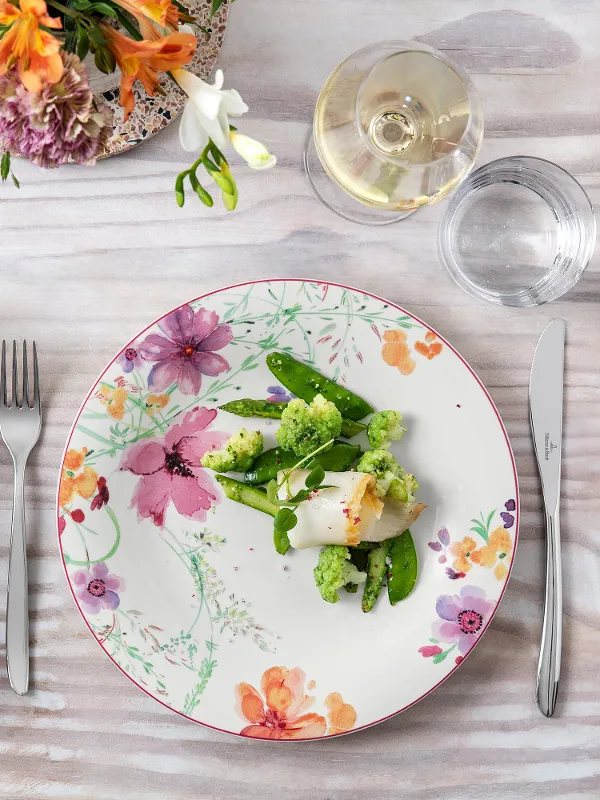 Elegant dining table with a floral-patterned Mariefleur plate, a healthy meal and a glass of white wine.