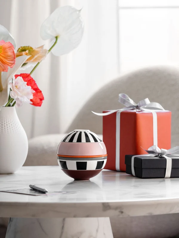 La petite Boule Memphis and two wrapped gifts stand on a table. La petite Boule Memphis from Villeroy & Boch and two wrapped gifts stand on a marble table, with a vase of flowers in the background.