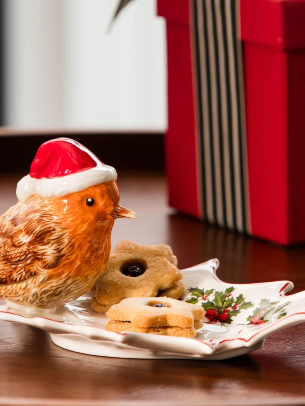 Toy's Fantasy bird On a festively designed Villeroy & Boch plate are a bird figurine with a Christmas hat and some cookies, next to it are a wrapped gift and a glass vase.