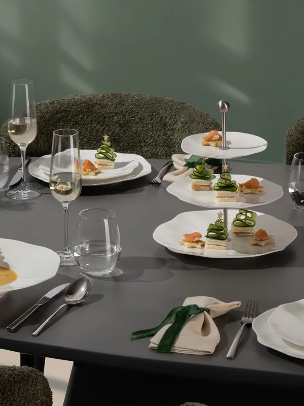 Una mesa de comedor Pura moderna puesta para cuatro personas, con platos gourmet, copas de vino y un arreglo floral verde como decoración de mesa.