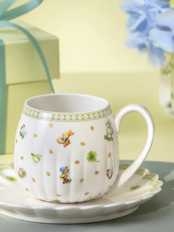 Easter Delight teacup on a Easter Delight saucer with a gift box and a vase of blue flowers in the background.