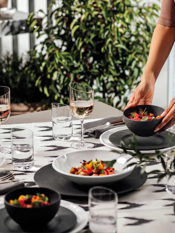 A woman setting a table with NewMoon and Manufacture plates and bowls for a barbecue evening outdoors.