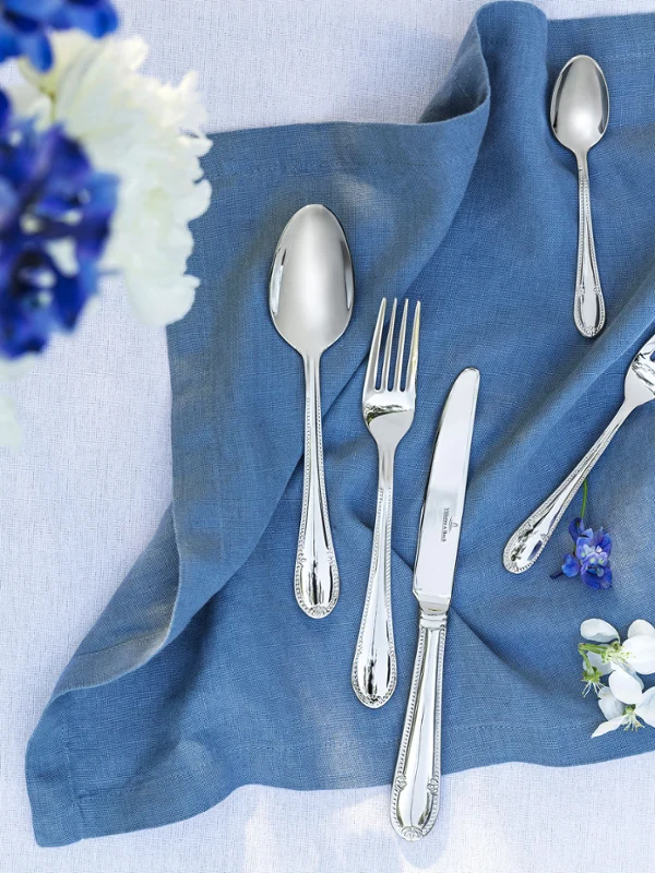 Stijlvolle tafeldecoratie met Mademoiselle bestek op een blauw linnen servet en een boeket bloemen.