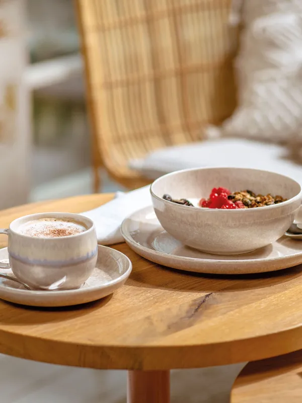 A Perlemor cup with coffee and a bowl of muesli on a wooden table.