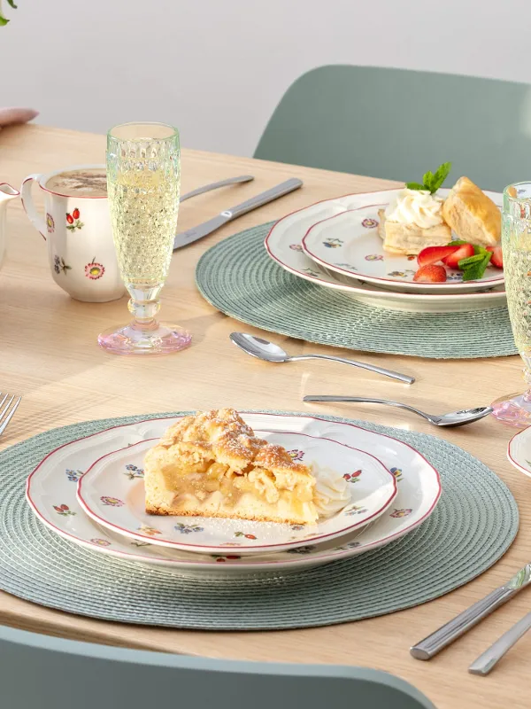A set table for two with dessert plates, teacups, a teapot, champagne glasses, and floral-patterned porcelain from Petite Fleur.