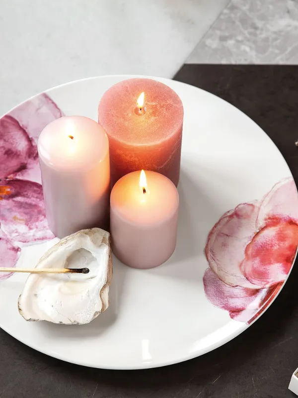 Decorative Rose Garden plate with lit candles next to a shell and a book with a gold leaf pattern.