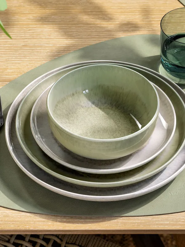 A table set with green and beige crockery, a bowl, a glass, cutlery and a green placemat.