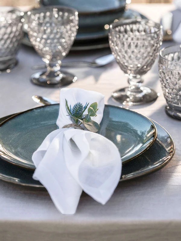 Stylish outdoor table setting with Lave plates and Boston glasses Lave plate outdoors with Boston glasses on a wooden table, accentuated with a white napkin and a sprig of greenery.