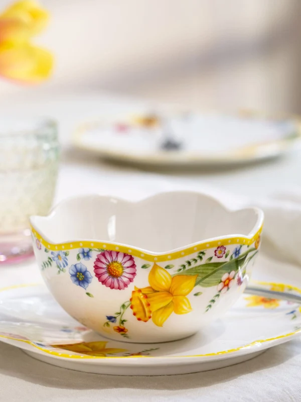 La tasse à thé et la soucoupe « Spring Awakening » avec cuillère de Villeroy & Boch. La tasse à thé et la soucoupe « Spring Awakening » avec cuillère de Villeroy & Boch sont posées sur la table, à côté de verres en cristal et de fleurs doucement floues en arrière-plan.