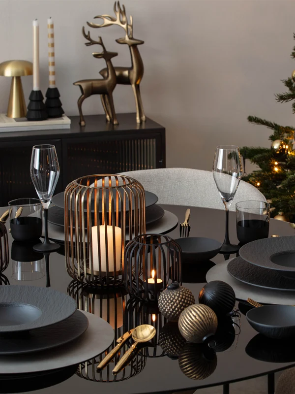 A black dining table set with dark crockery A black dining table set with dark crockery, Christmas decorations, candles and an illuminated Christmas tree in the background.