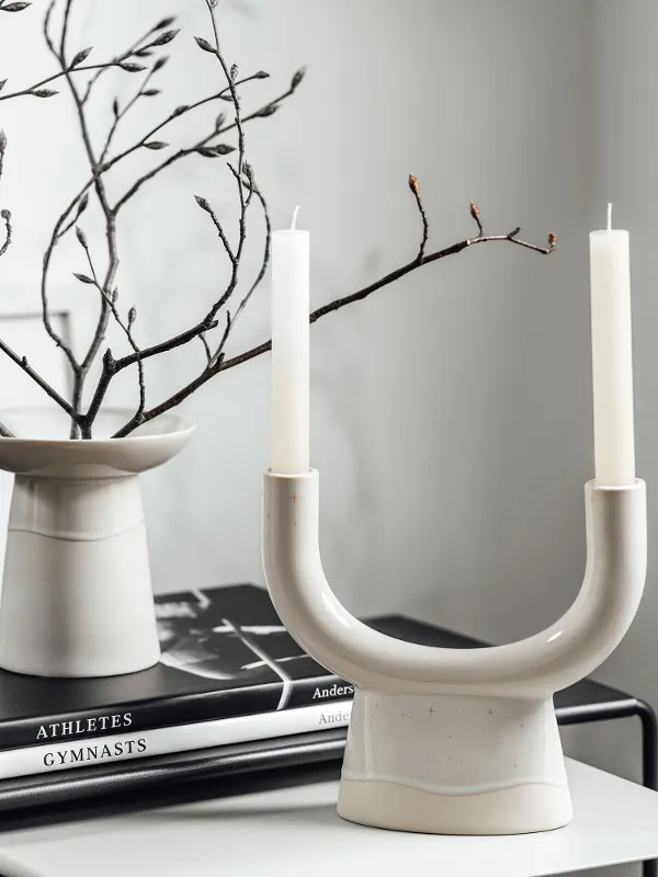 Two candles in a Winter Glow candleholder beside a Winter Glow vase on a table.