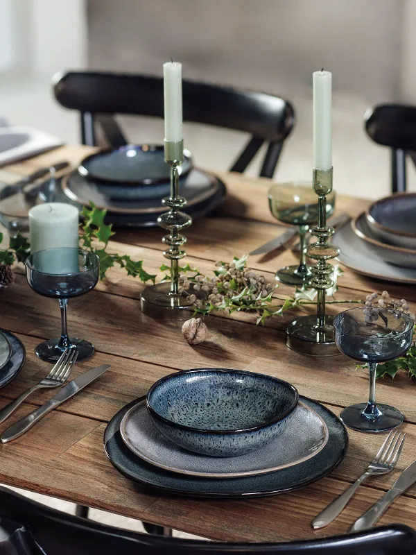 Elegantly laid dining table with Villeroy & Boch Lave plates, glasses, candles and green plants on a wooden surface.