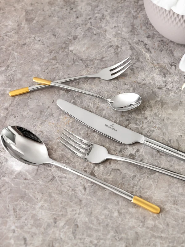 Zestaw sztućców Ella ze złotymi akcentami marki Villeroy & Boch Elegancki zestaw sztućców Ella ze złotymi akcentami na marmurowym blacie, w towarzystwie białej orchidei.