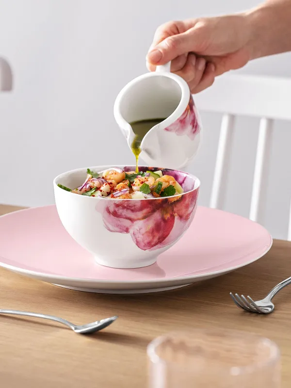 A person pouring dressing over a salad in a Rose Garden bowl at an elegantly laid dining table with Rose Garden crockery.