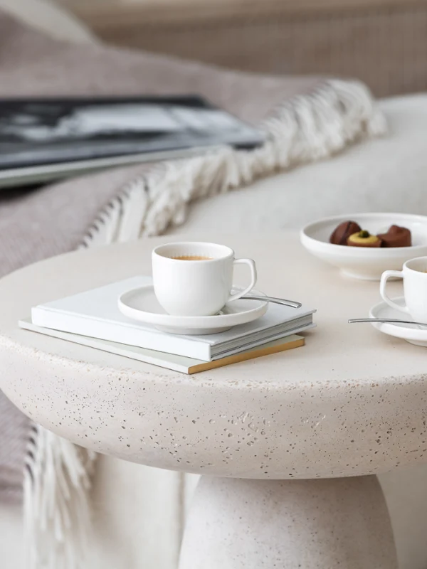 Two elegant Afina espresso cups on a round table with a magazine and a plate of chocolates.