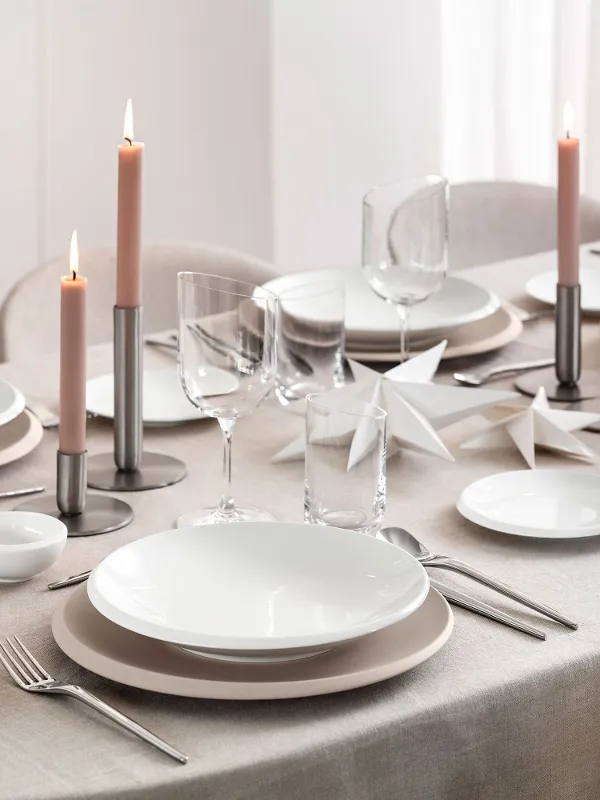 Vue de dessus d’une table festive moderne avec la collection NewMoon Beige de Villeroy & Boch : bol plat, assiettes de dîner et à pain, associés aux couverts NewMoon, verres à vin et gobelets. De doux accents décoratifs de Noël – tels que des ornements clairs, des branches de pin ou des bougies – apportent une touche saisonnière raffinée aux tons naturels et aux formes minimalistes.