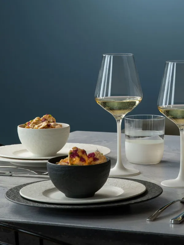 Elegant dinner with two white wine glasses, neatly arranged Manufacture plates and bowls with food on a modern table.