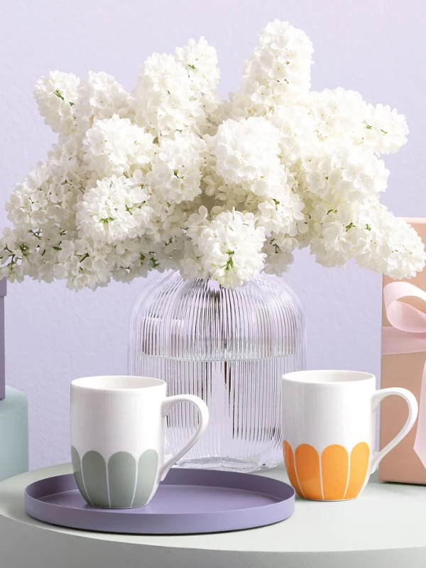 Cztery filiżanki Fleur od Villeroy & Boch Filiżanki Fleur od Villeroy & Boch w pastelowych kolorach, wazon Fleur, pudełka prezentowe i biały wazon z kwiatami na delikatnie stonowanych powierzchniach.