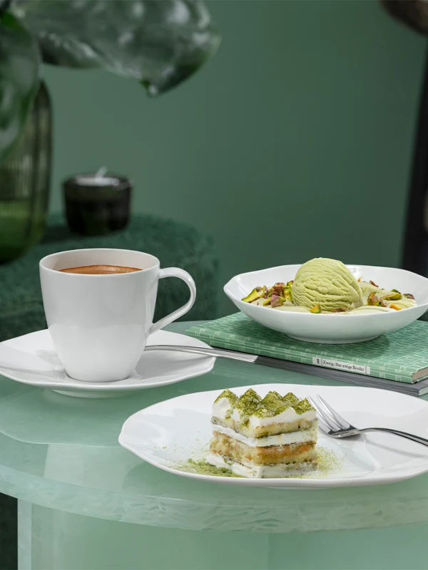 Eine Pura Kaffeetasse , ein Stück Kuchen und eine Pura Dessertschale stehen auf einem Glastisch Eine Pura Kaffeetasse , ein Stück Kuchen und eine Pura Dessertschale mit Eis stehen auf einem Glastisch mit einer Grünpflanze im Hintergrund.