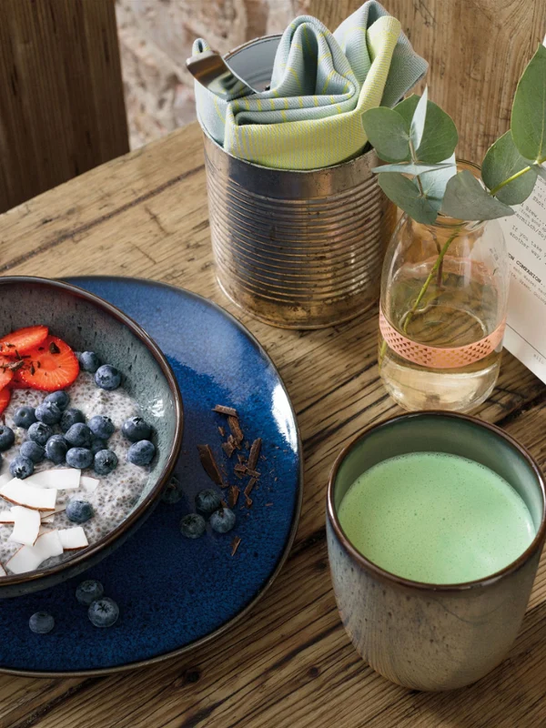 Een gezonde smoothie bowl op een houten tafel in een Lave kom, een Lave beker matcha latte en een menukaart.