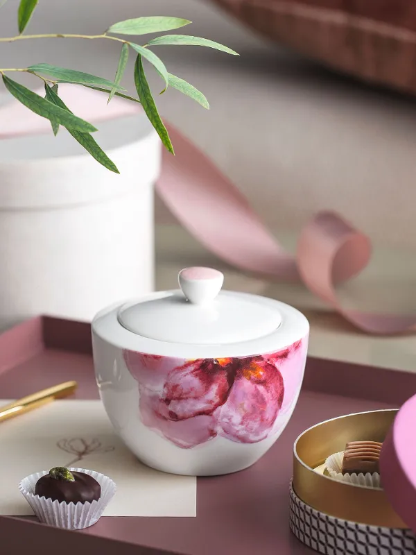 A Rose Garden sugar bowl with a candle, a gold spoon, a chocolate truffle and decorative items on a tray.