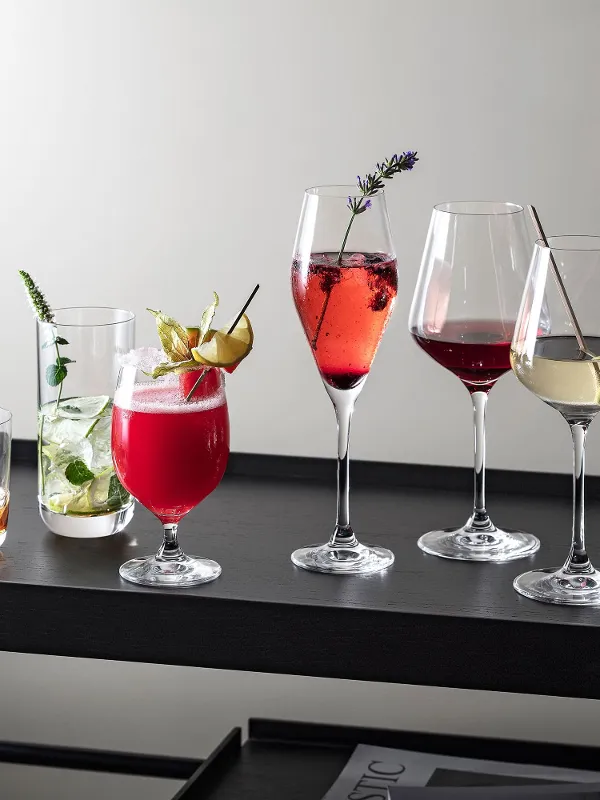 Various drinks in La Divina glasses presented on a modern black tray, decorated with herbs and fruit.