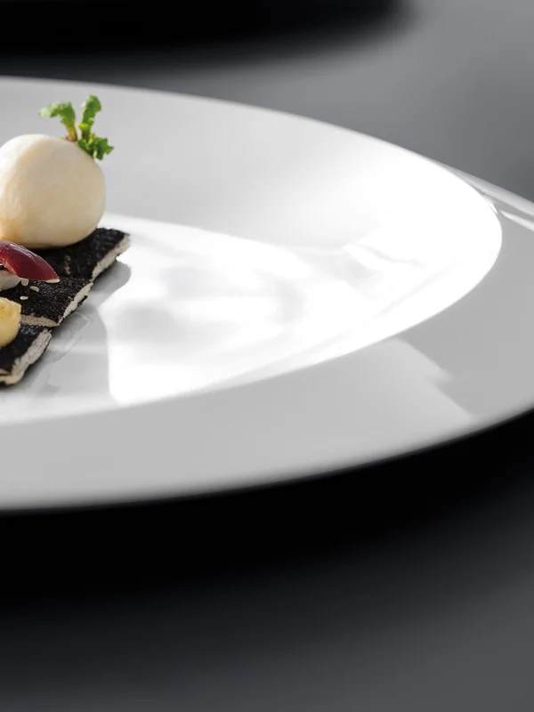 Ein weißer Teller mit Crackern, belegt mit Käse und Oliven, und einer kleinen Käsekugel, garniert mit einem Zweig Petersilie.