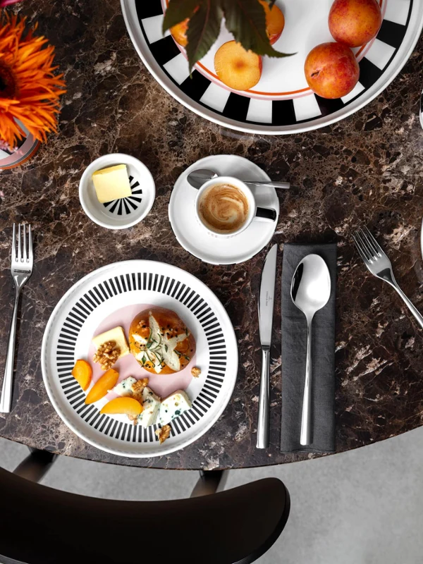 Extravagant Memphis table setting Top view of a marble table with fruit, coffee, cereal, and yogurt bowls from the Memphis collection by Villeroy & Boch, cutlery, and floral decorations.