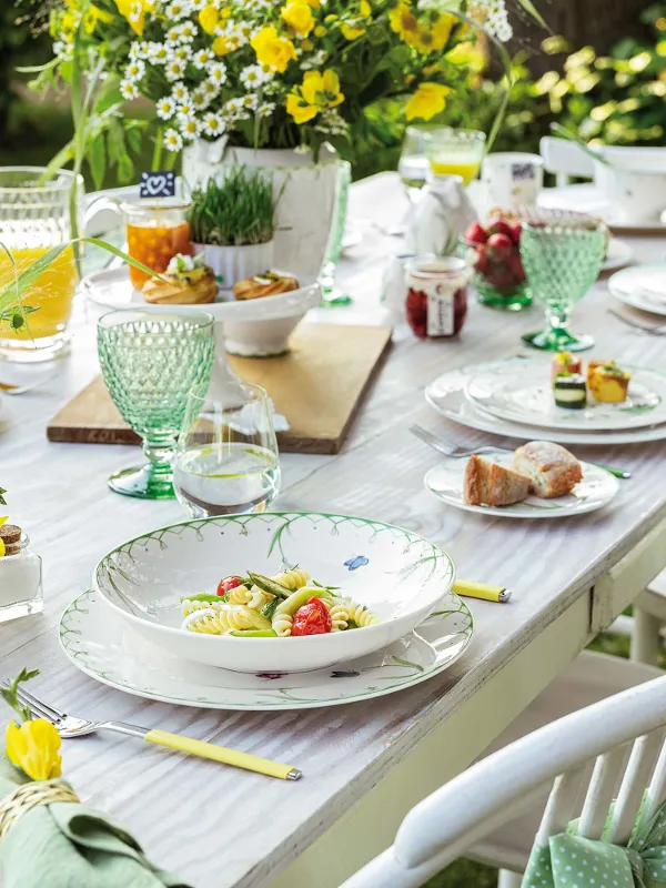 An elegantly set dining table with Colourful Spring outdoor dinnerware with a spring theme, decorated with fresh flowers and ready for a meal in the garden.