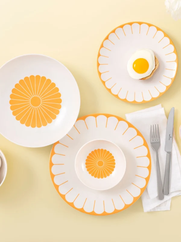 Service de table avec assiettes Fleur Soleil de Villeroy & Boch Service de table avec assiettes Fleur Soleil de Villeroy & Boch, œufs, thé avec une tranche de citron et fleurs blanches sur un fond jaune clair.