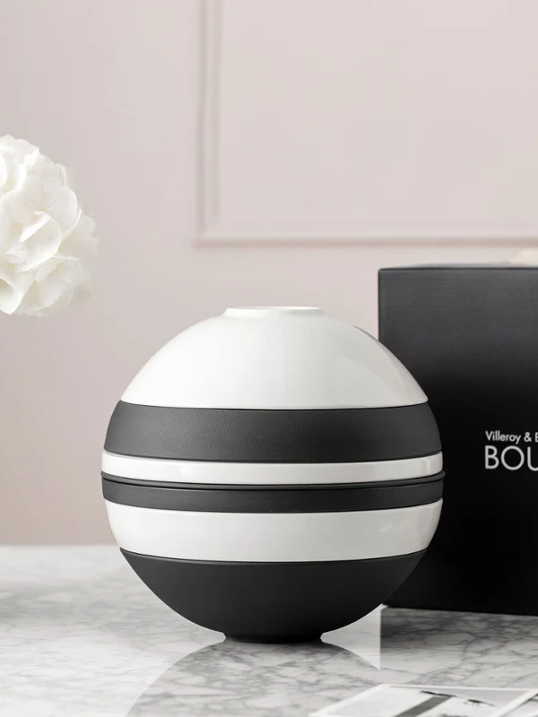 Una La Boule in bianco e nero di Villeroy & Boch si trova su una superficie di marmo, accompagnata da un vaso bianco con un fiore e da una scatola nera aperta con la dicitura "La Boule".