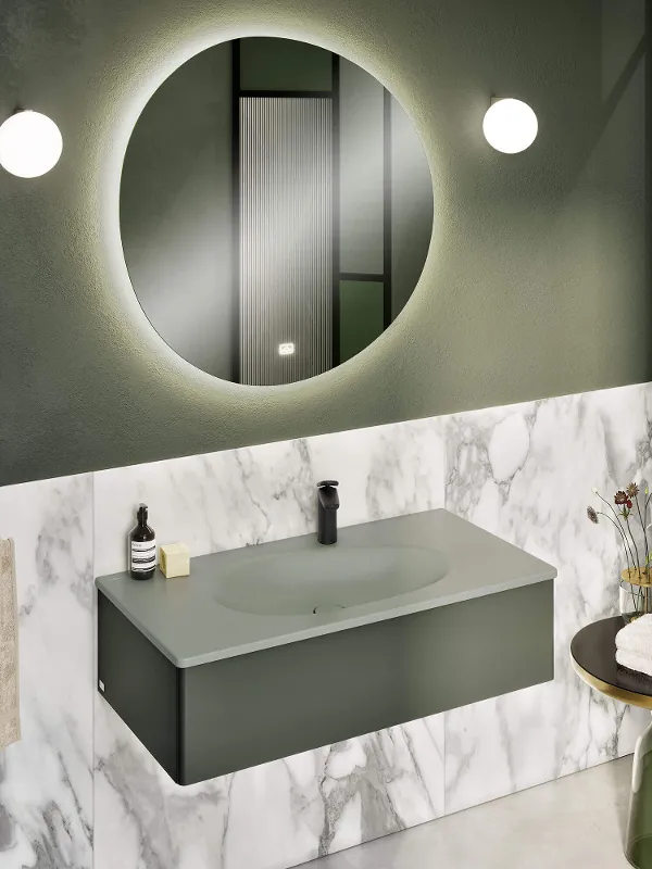 A green Antao vanity washbasin in the bathroom with a round mirror and green walls.