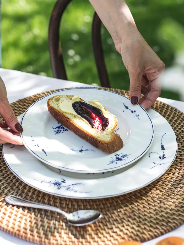 A person placing an Old Luxembourg plate, with fruit spread and butter, on a woven placemat.