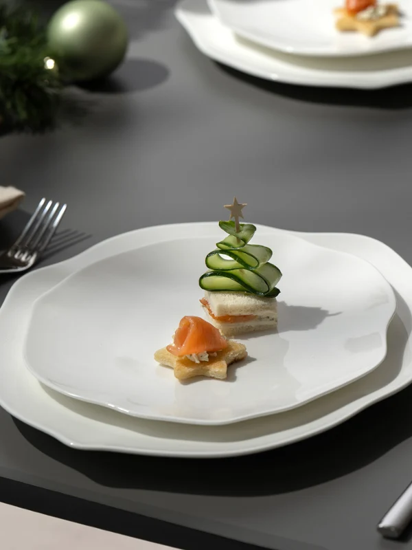 Un plato Pura blanco con pequeños aperitivos, incluyendo una torre de pepino, en una mesa puesta con decoración festiva.