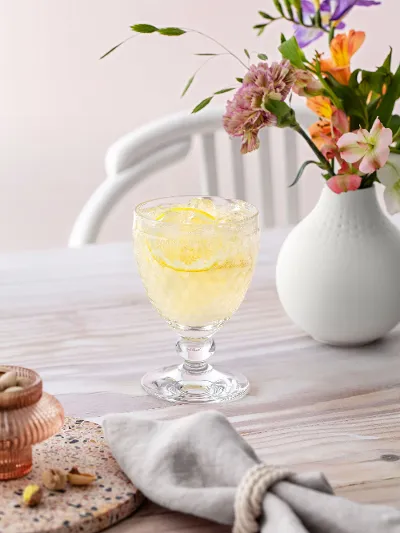 A chilled drink in a Boston glass on a table next to a white vase with colorful flowers.