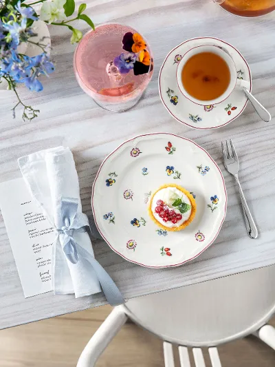 Petite Fleur plate with a cake, a teacup, a drink with a flower and a napkin on a wooden table.