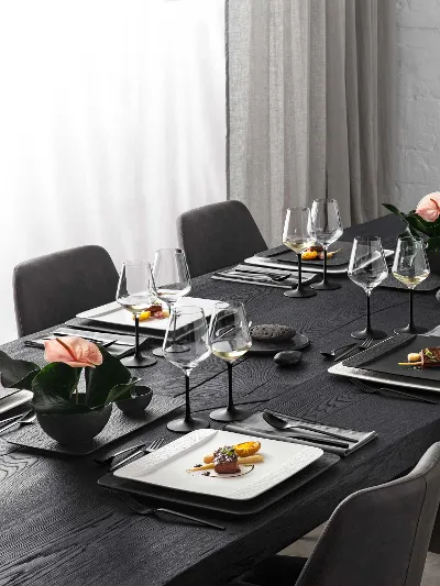 A black table in an elegant living room set with glasses, rectangular crockery and cutlery from the Villeroy & Boch Manufacture collection.