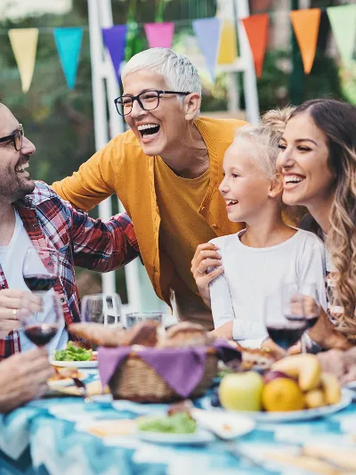 People laughing together at a table Six people are sitting around a table, laughing. Colorful pennants are decorating the background.