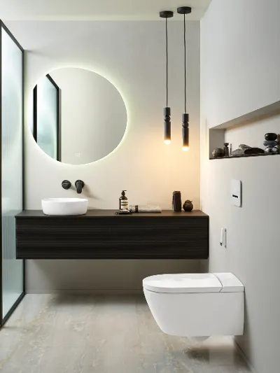 Antao collection bathroom with a ViClean shower toilet from Villeroy & Boch Modern bathroom with a wall-mounted toilet, a floating black washstand with a white washbasin, an illuminated round mirror, hanging lamps and a frosted glass partition.