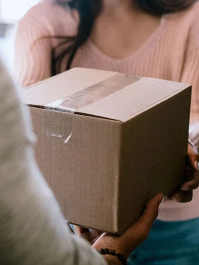 A person hands a box to another person in a doorway.
