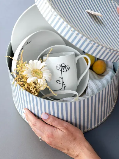 A round box with a Villeroy & Boch floral-patterned Statement crockery set with a cloth, a margarita flower and apricots as a gift.