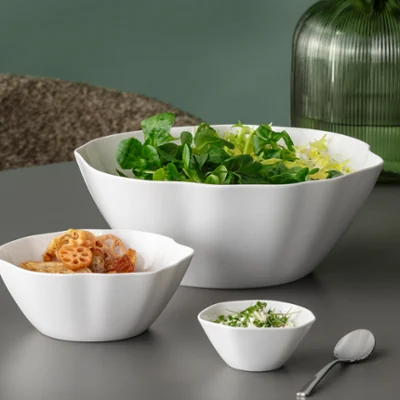 Three white Pura bowls with salad, pasta and herbs Three white Pura bowls with salad, pasta and chopped herbs on a grey table, with green vases in the background.
