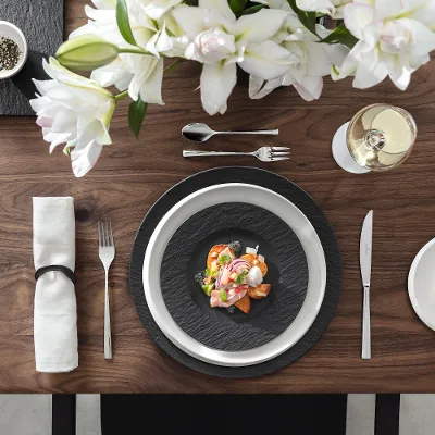 Elegante Tischdekoration mit einem Meeresfrüchtegericht auf Manufacture Tellern, weißen Blumen, einem Glas Weißwein und einem kleinen Teller mit Zitronenscheiben.