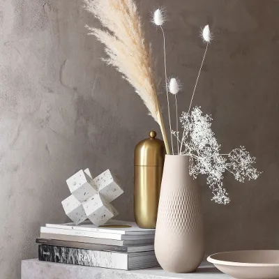 A table with a beige Manufacture vase and a NewMoon plate on top.