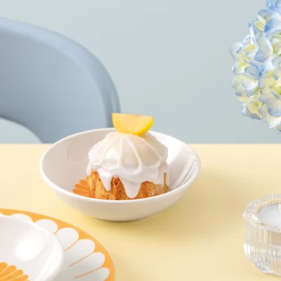 A yellow Fleur bowl with a tarte on a light yellow table next to a flower arrangement.
