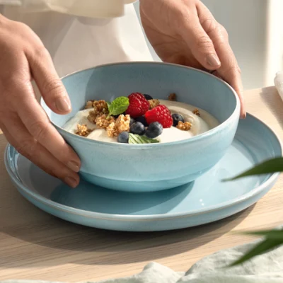 Hands placing a blue mother-of-pearl aqua bowl with yoghurt on a blue plate Hands placing a blue mother-of-pearl aqua bowl with yoghurt, muesli, blueberries and raspberries on a blue plate.