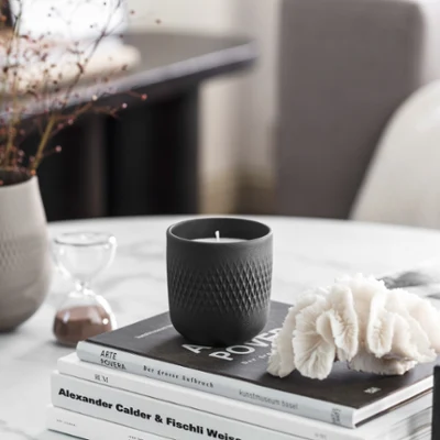 Une bougie parfumée Manufacture et un vase sur une table en marbre Une élégante composition de décoration intérieure avec une bougie parfumée Manufacture noire, des livres et un vase Manufacture gris clair sur une table en marbre.