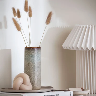 Tall beige Lave vase on a shelf A shelf with a tall beige Lave vase and a lamp on top.